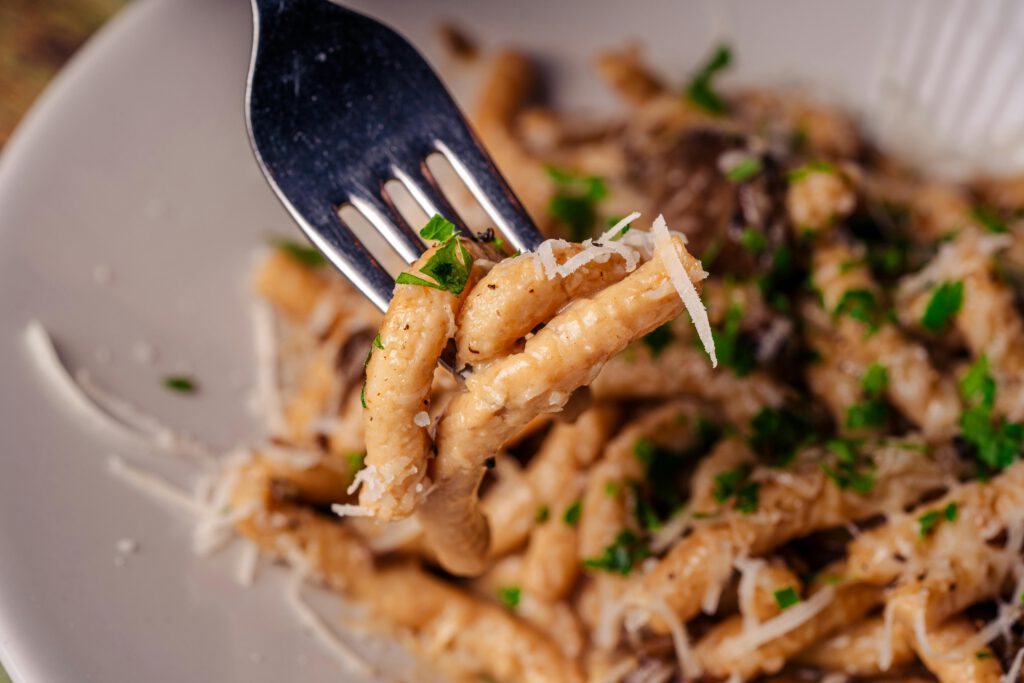 A tantalizing close-up of pasta on a fork with fresh herbs and cheese, perfect for a gourmet meal.